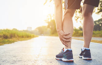 Injury from workout concept   The asian man use hands hold on his ankle while running on road in the park  Focus on ankle 